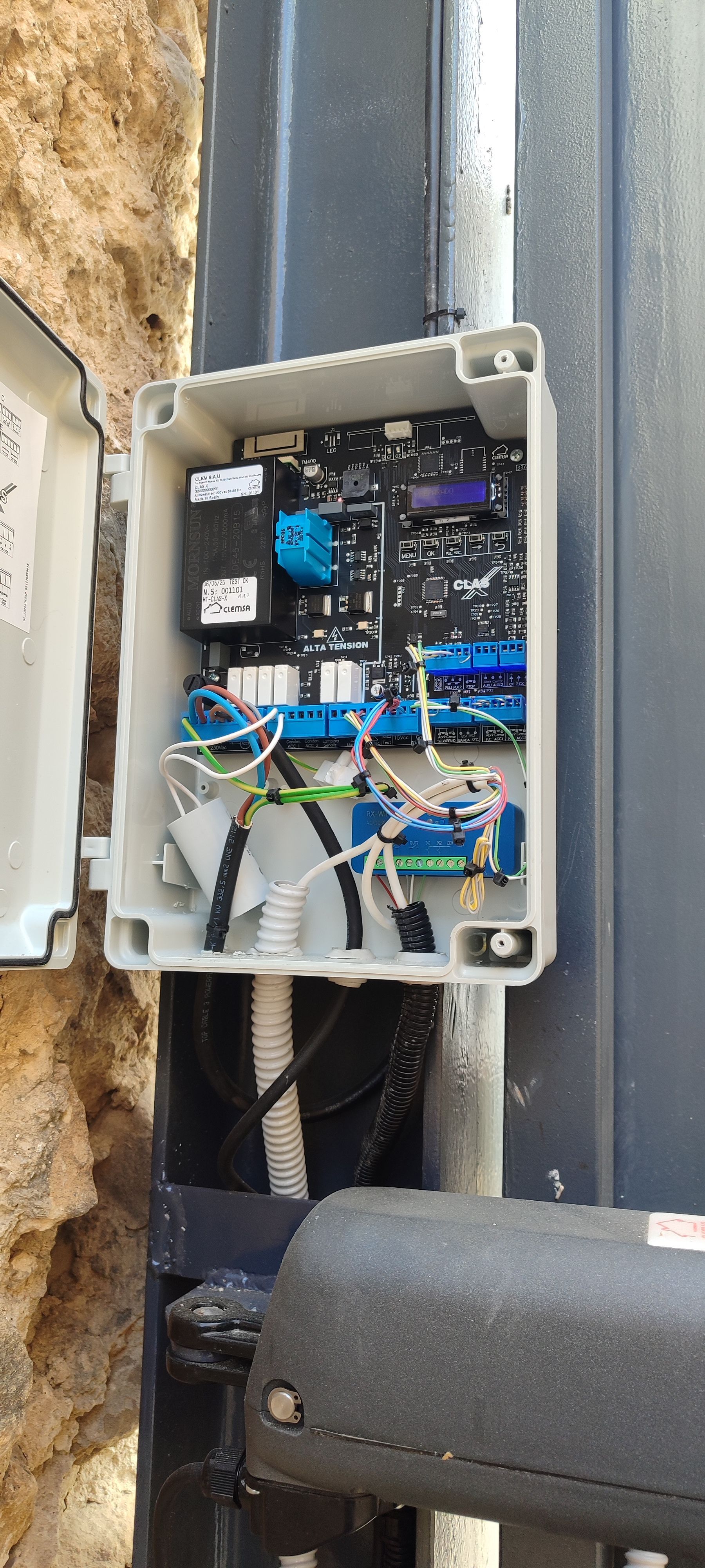 Una caja eléctrica blanca abierta, montada sobre un poste metálico. Contiene placas de circuitos, cables y otros componentes electrónicos.