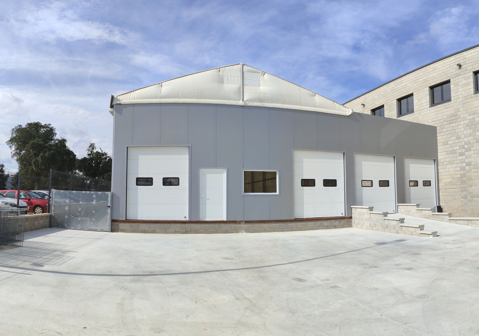 Nave industrial gris con tres puertas de garaje y una pequeña ventana bajo un techo blanco.