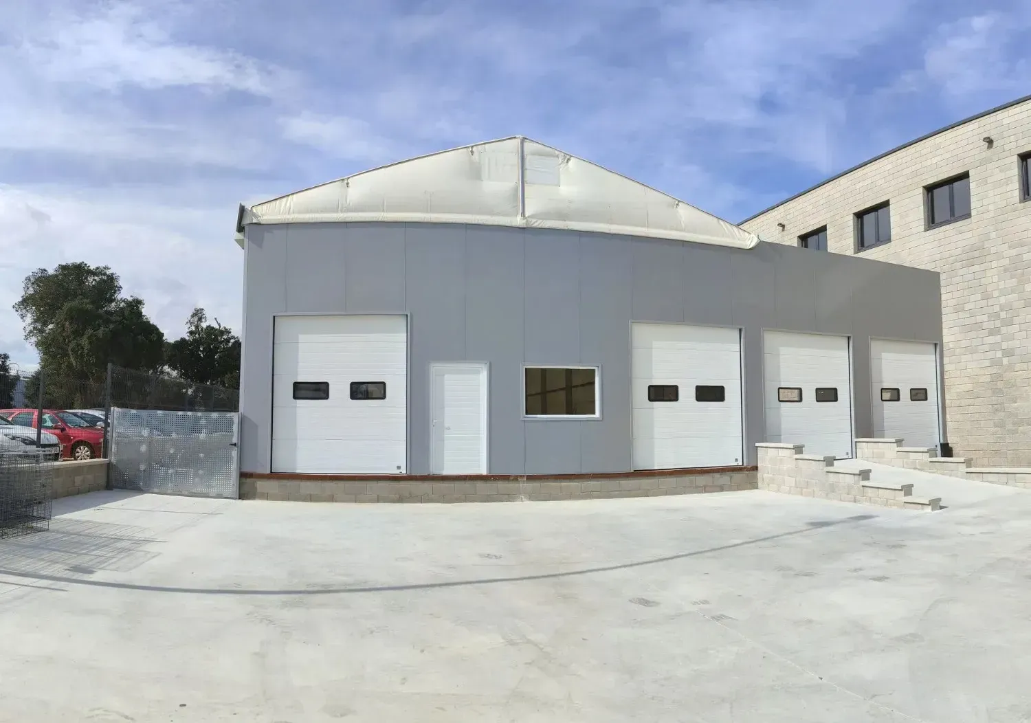 Nave industrial gris con tres puertas de garaje y una pequeña ventana bajo un techo blanco.