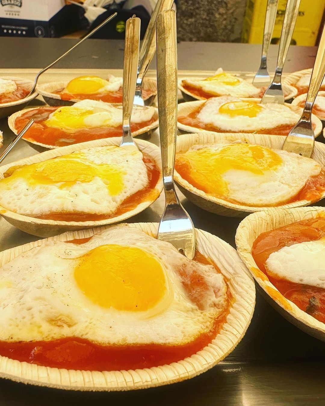 Un montón de huevos fritos en salsa de tomate con tenedores.