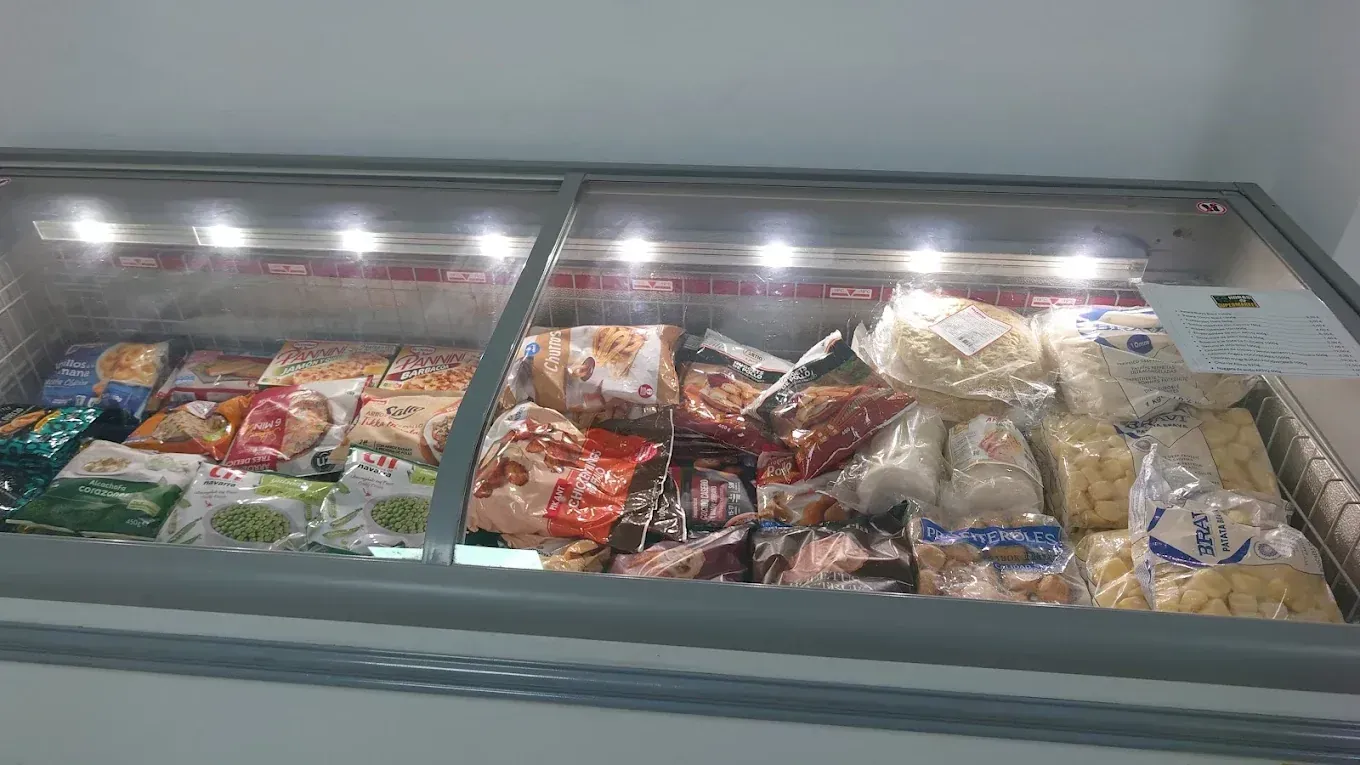 Congelador lleno de diversos paquetes de alimentos congelados bajo luces brillantes.