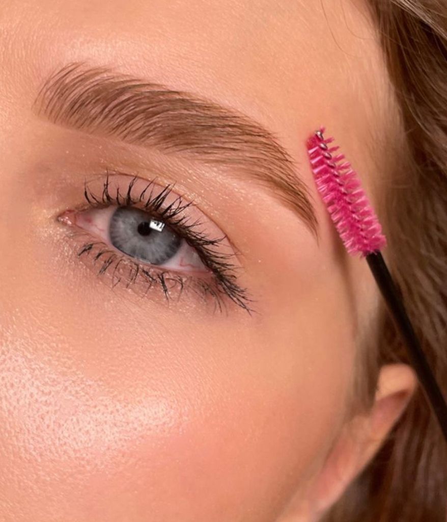Eine Person in schwarzen Handschuhen trägt mit einem Kosmetikinstrument präzise Make-up oder Microblading im Bereich der Augenlider einer Kundin auf.