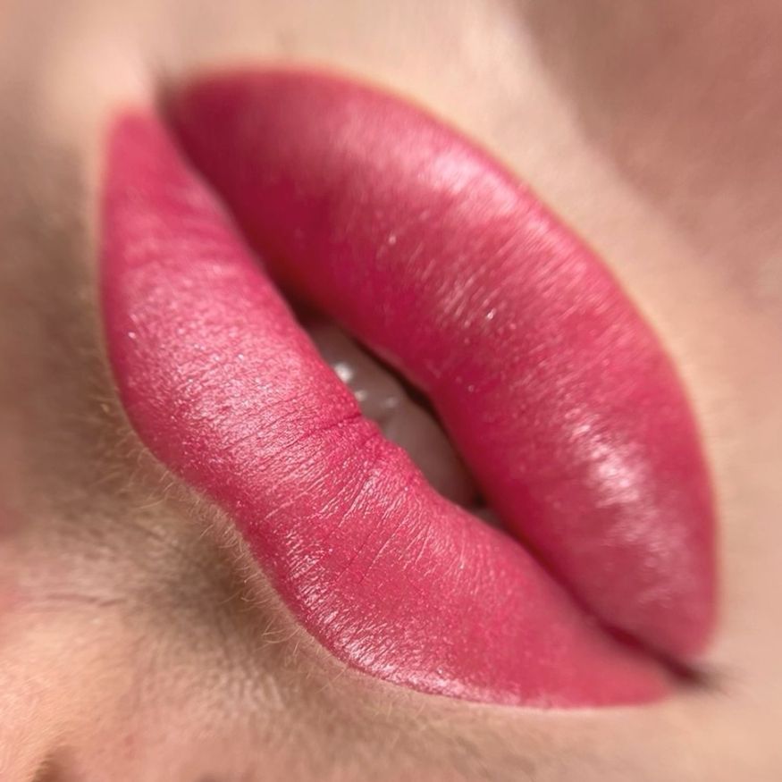 Nahaufnahme einer Person, die von einer Technikerin mit schwarzen Handschuhen eine kosmetische Lippentätowierung erhält.