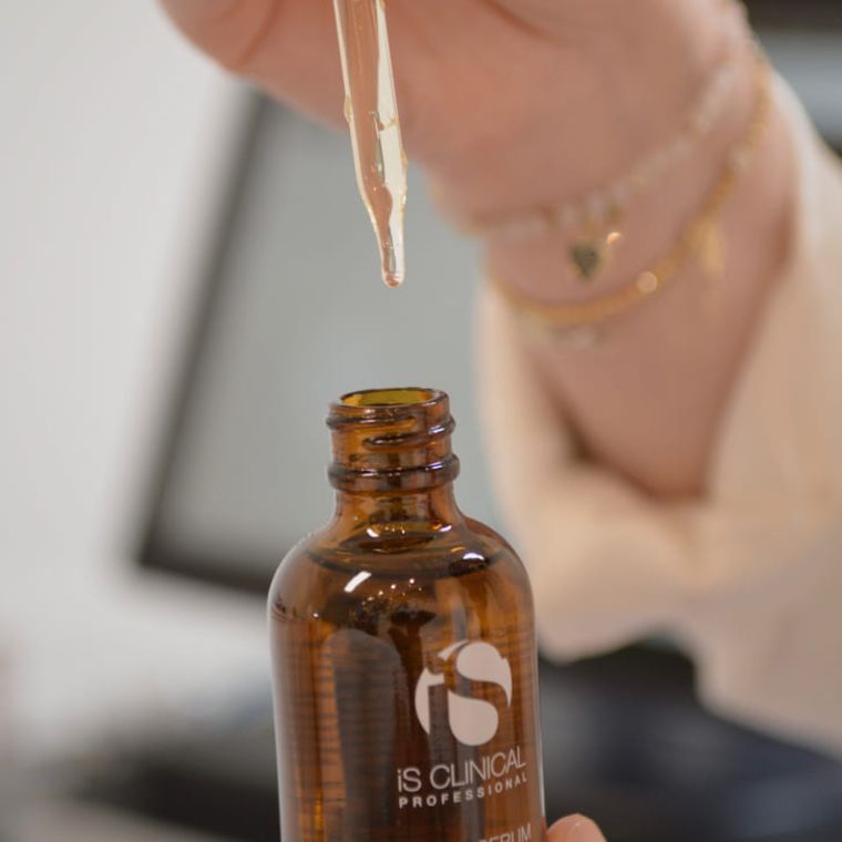 Eine Glaspipette gibt eine klare Flüssigkeit in eine bernsteinfarbene Flasche iS CLINICAL Hautpflege-Serum ab.