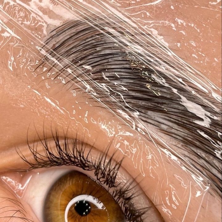 Nahaufnahme einer mit durchsichtiger Plastikfolie bedeckten Augenbraue, darunter ist ein Teil langer, geschwungener Wimpern sichtbar.