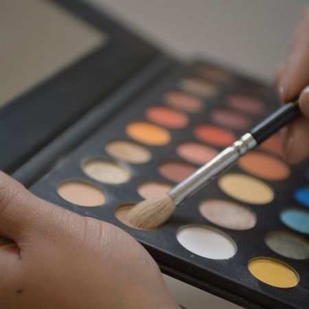 Ein Schminkpinsel wird in einen runden Tiegel mit Lidschatten aus einer mehrfarbigen Schminkpalette getaucht.