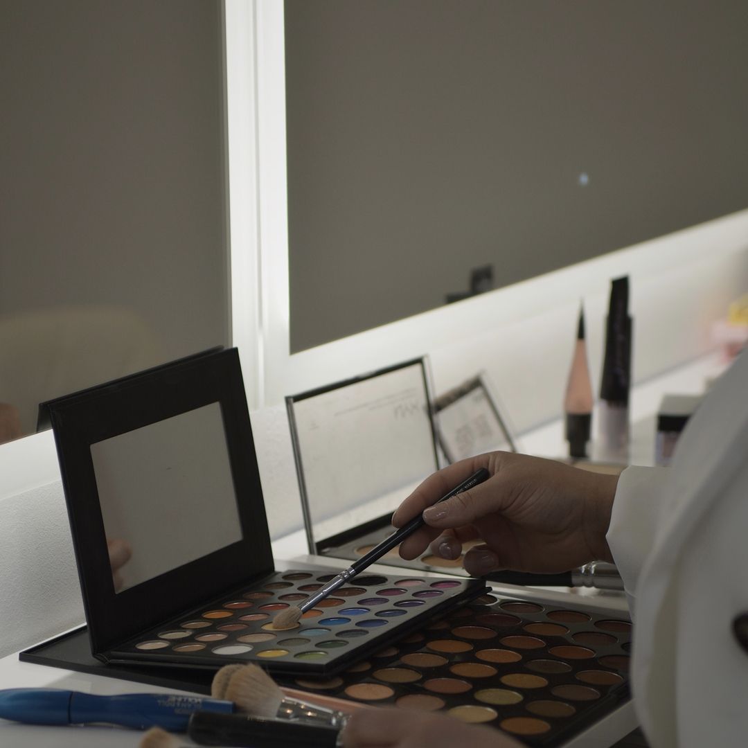 Eine Person in schwarzen Handschuhen trägt mit einem Kosmetikinstrument präzise Make-up oder Microblading im Bereich der Augenlider einer Kundin auf.