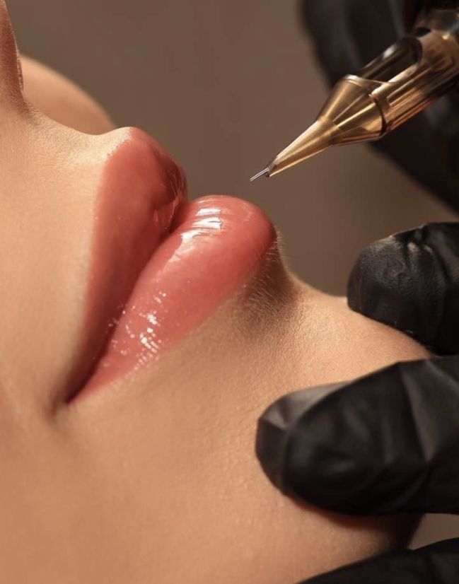 Nahaufnahme einer Person, die von einer Technikerin mit schwarzen Handschuhen eine kosmetische Lippentätowierung erhält.