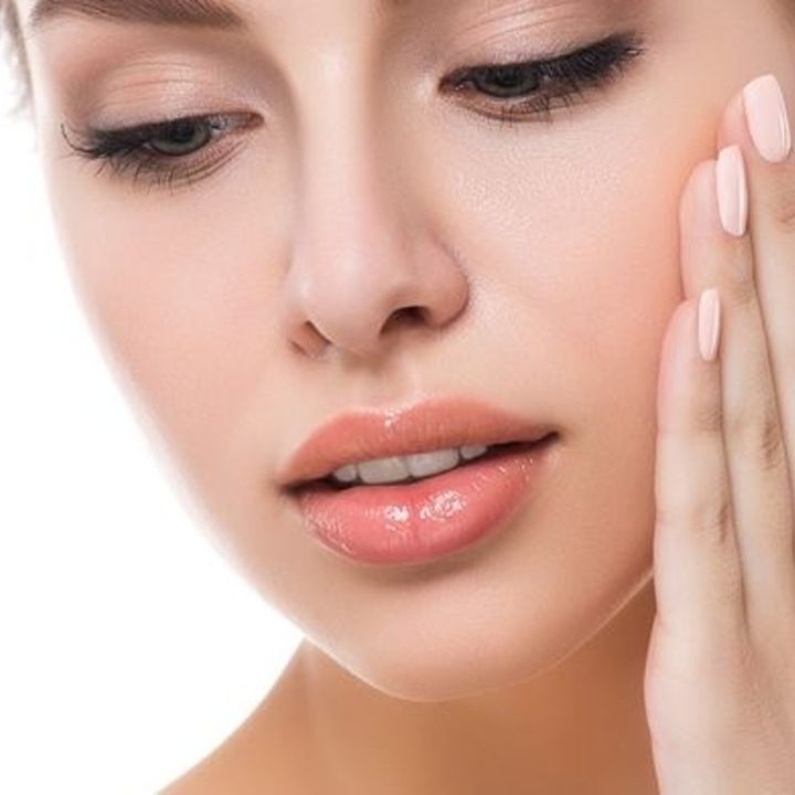 Nahaufnahme einer Person, die sich mit der Hand an die Wange fasst; die Haut ist glatt, rein und das Make-up natürlich.