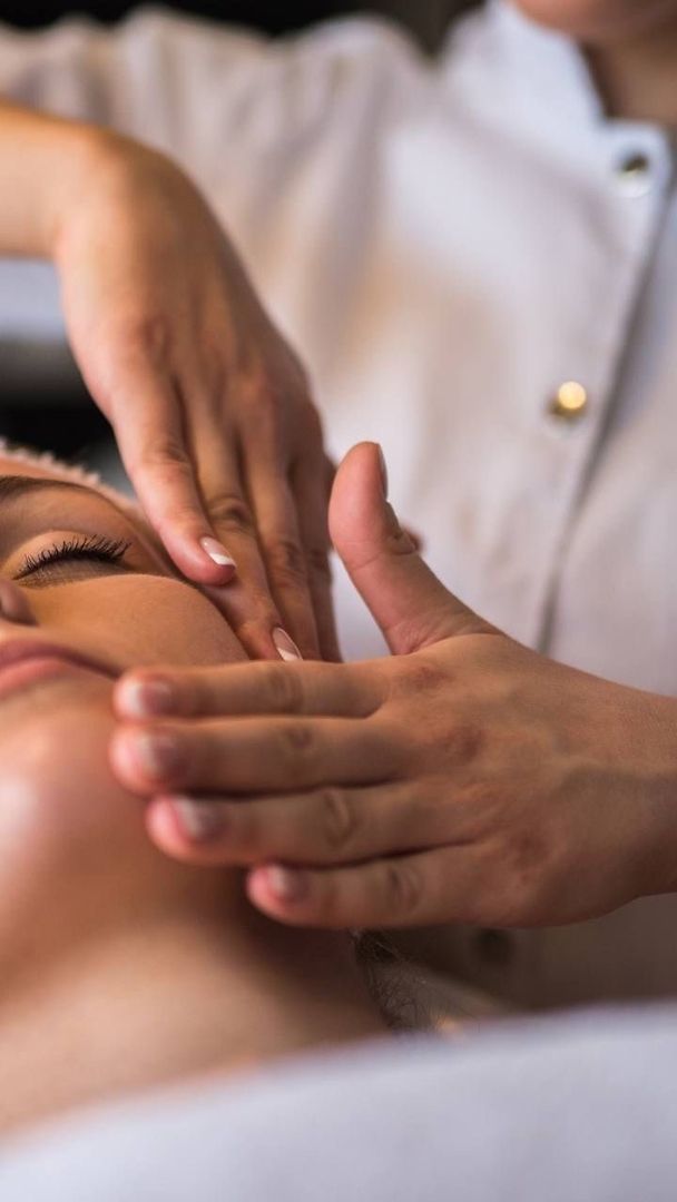 Eine professionelle Gesichtsbehandlungssequenz, die eine Produktflasche, das Auftragen von Tropfen auf die Haut und die Massage des Gesichts eines Kunden zeigt.