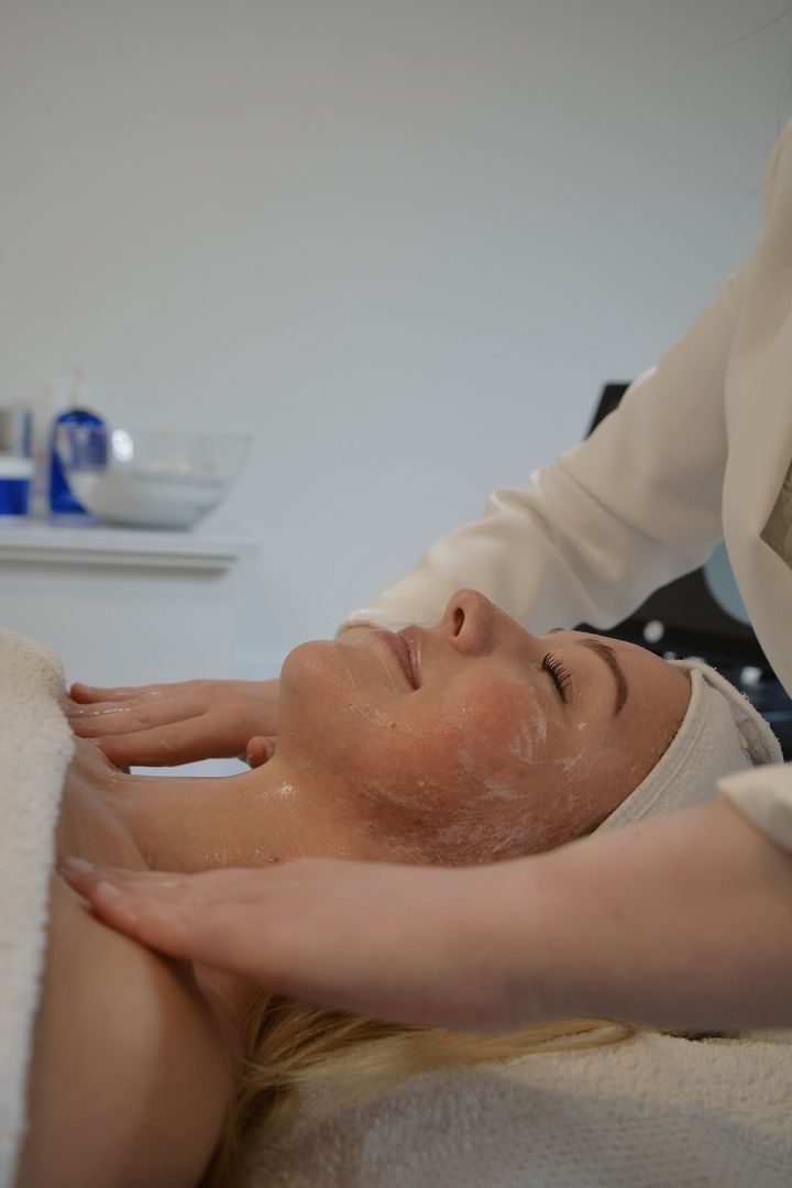 Eine Person genießt eine entspannende Gesichtsmassage in einem Spa, bei der die Hände eines Therapeuten sanft Produkte auf ihr Gesicht auftragen.