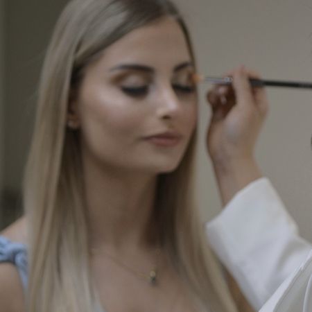 Eine Person, die einer anderen Person mit einem Pinsel Make-up auf das Augenlid aufträgt.