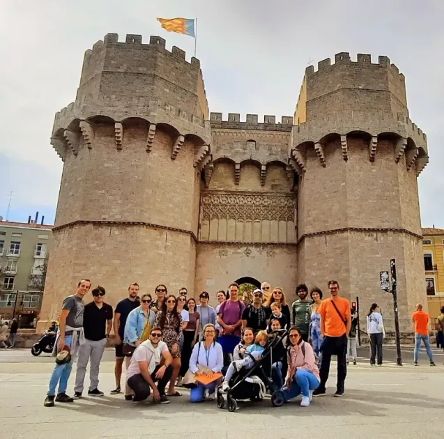 Grupo posando frente a la puerta de piedra de un castillo histórico con dos torres y una bandera en lo alto.