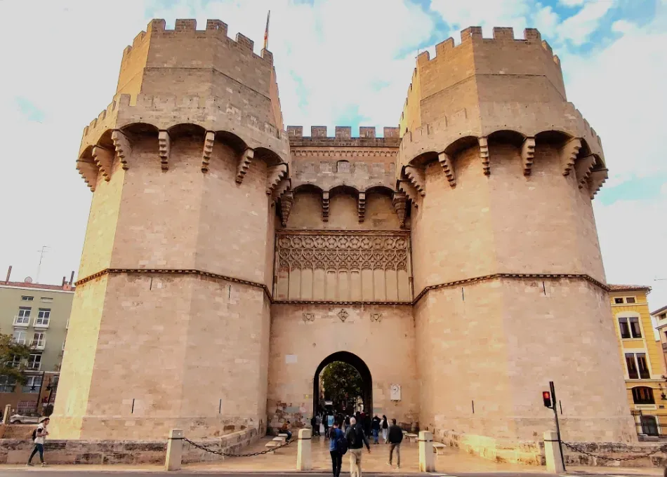 Histórica puerta de piedra de la ciudad con dos torres redondas y una entrada arqueada, vista desde el frente bajo un cielo pálido.