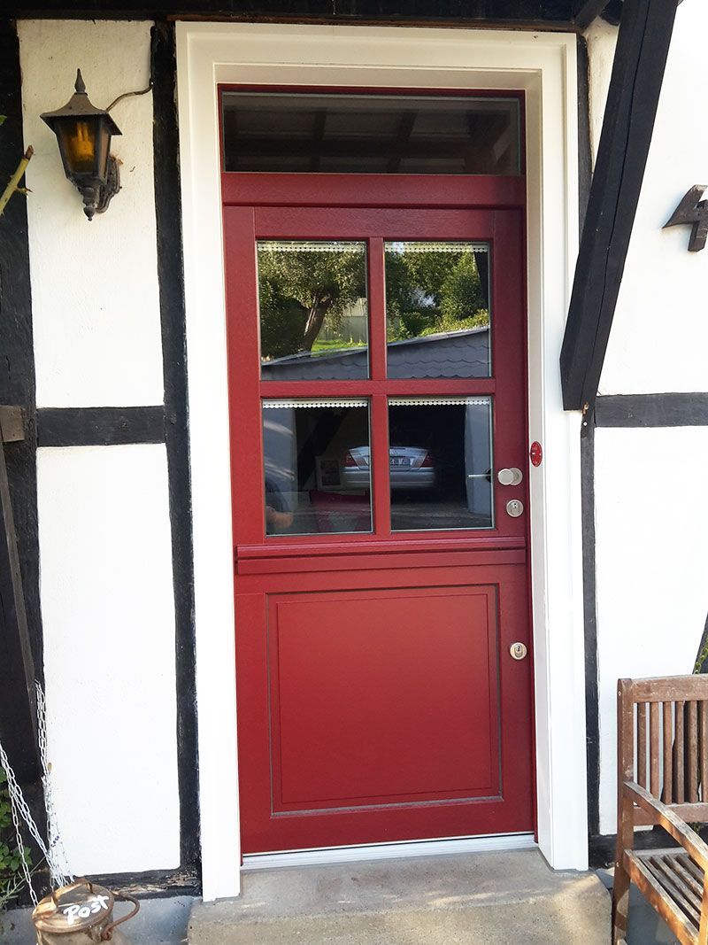 Auf einer Veranda neben einer Bank steht eine rote Tür.