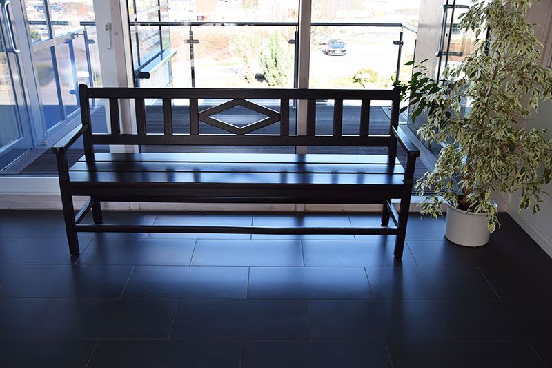 Eine Holzbank steht vor einem Fenster neben einer Topfpflanze.