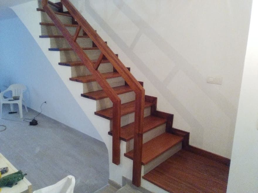 Escalera de madera con barandilla roja junto a una pared blanca en una habitación luminosa.