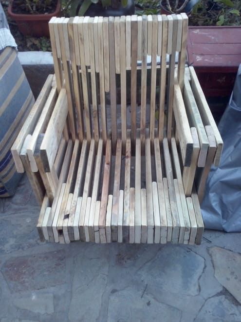 Silla de listones de madera con reposabrazos en un patio de piedra al aire libre.