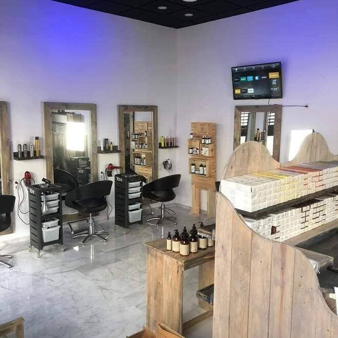 Interior de salón moderno con sillones de peluquería, espejos, estantes y expositores de productos.