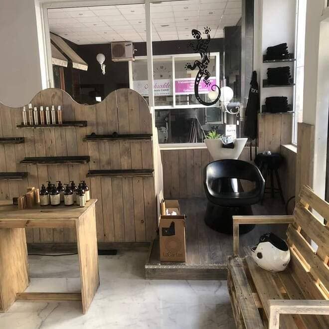 Interior del salón revestido de madera con estantes, bancos, una silla negra y una zona de mostrador con ventana.