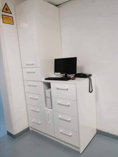 Un armario de oficina blanco con cajones y un pequeño monitor de ordenador en una habitación de la esquina.
