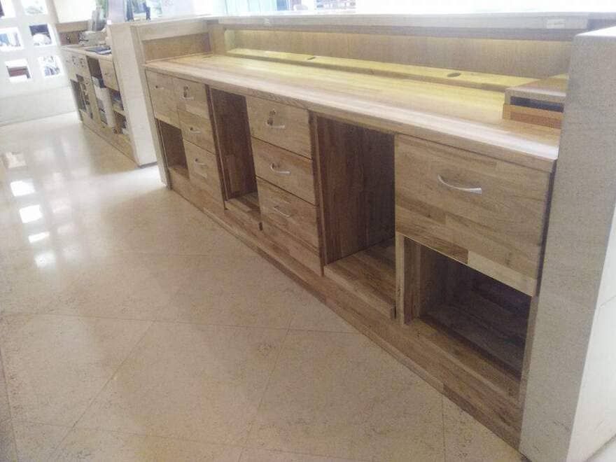 Mostrador expositor de madera con cajones y estantes abiertos en un pasillo de la tienda.
