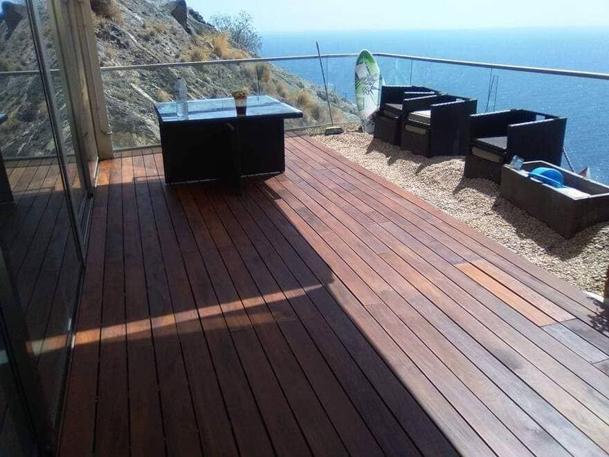 Terraza costera de madera con muebles de exterior negros con vistas al océano y a los acantilados rocosos.