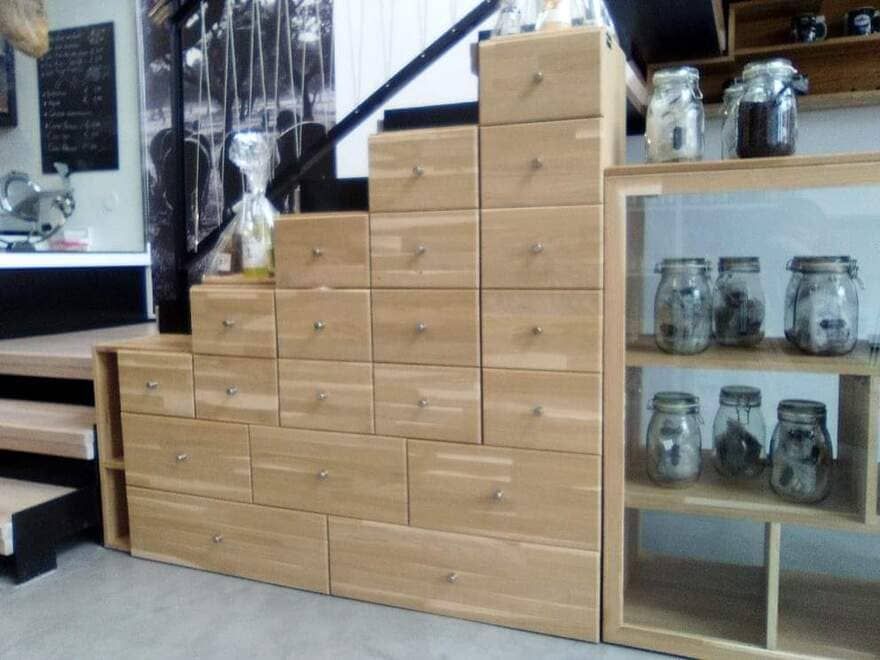 Cajoneras de madera apiladas que forman una escalera junto a una vitrina con tarros en una tienda o cafetería.