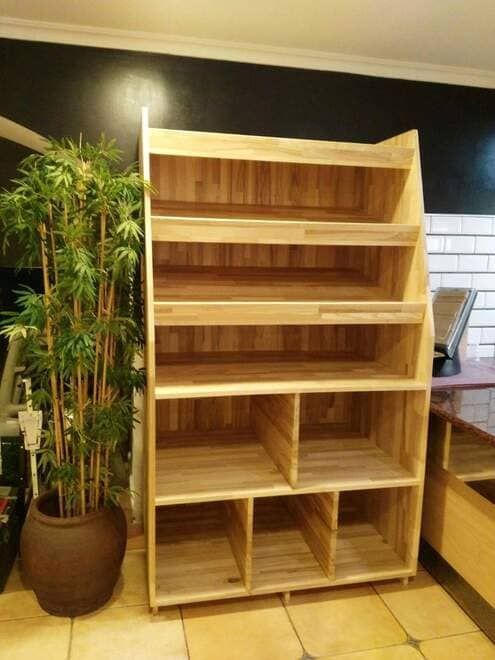 Estantería de madera con estantes abiertos junto a una planta alta de bambú en maceta, en el interior.