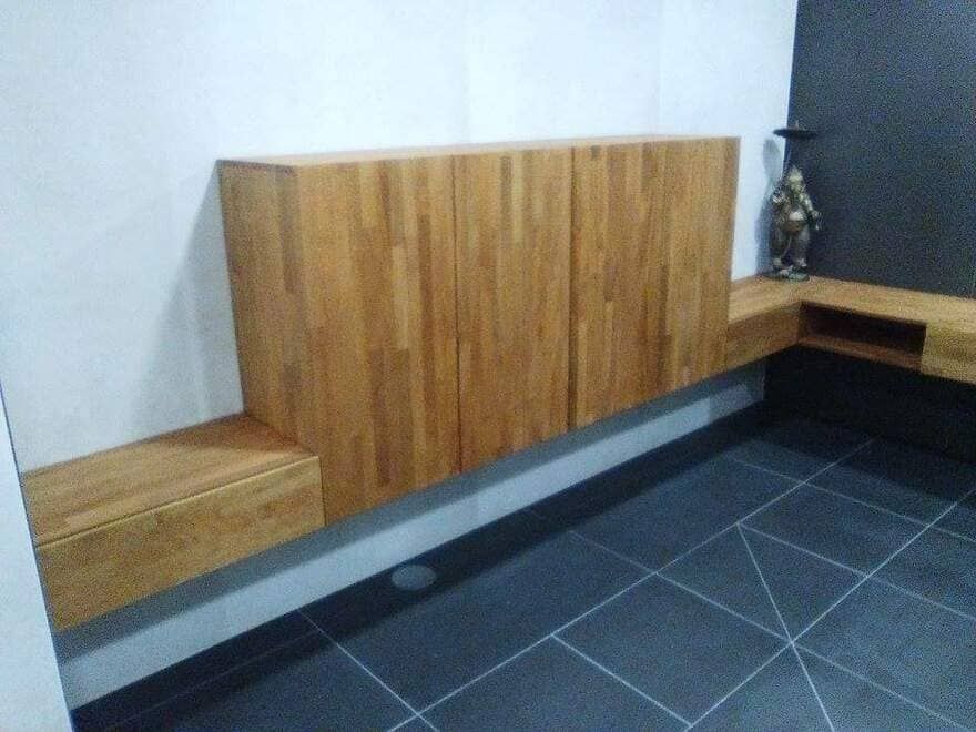 Banco de madera adosado a una pared en una habitación moderna con suelo de baldosas oscuras.