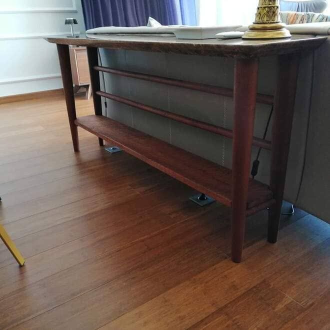 Escritorio de madera con paneles grises junto a un suelo de madera noble y cortinas en la ventana.