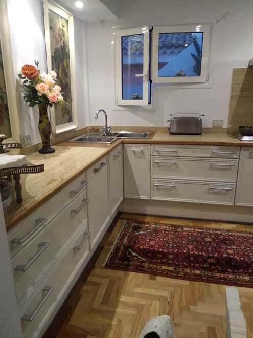 Cocina moderna con gabinetes blancos, encimeras de madera, ventana, fregadero y alfombra con estampado rojo.