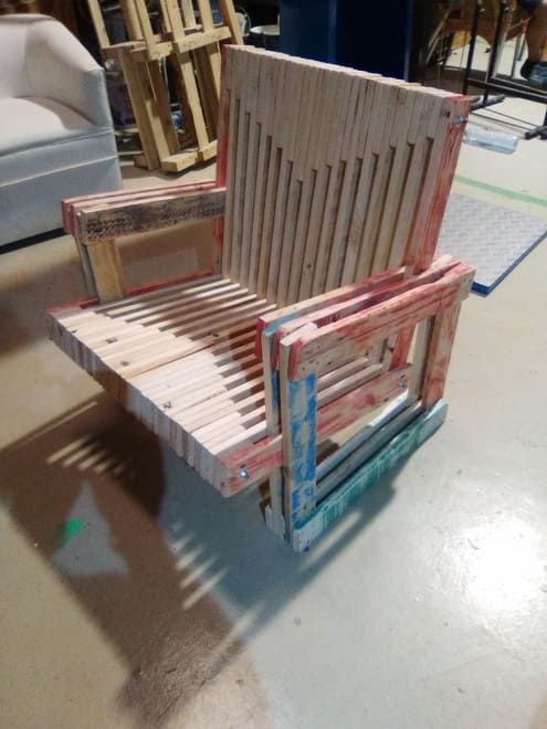 Silla de madera hecha a mano y pintada con rayas multicolores, colocada sobre el suelo de un taller.