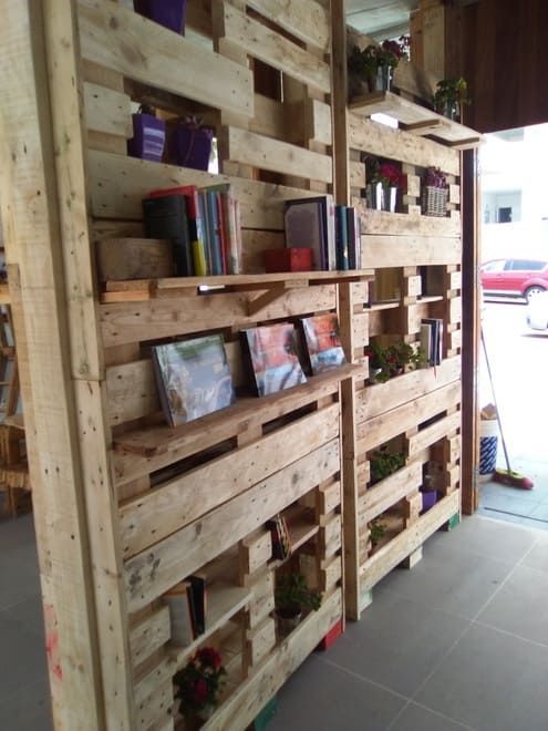Estantería de palets de madera con libros y pequeñas plantas en la entrada de una tienda rústica.