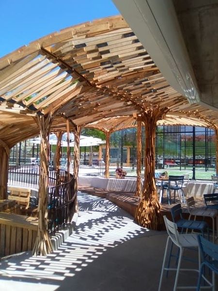 Zona de estar exterior sombreada con pérgola de madera, mesas, sillas y vistas a la piscina.