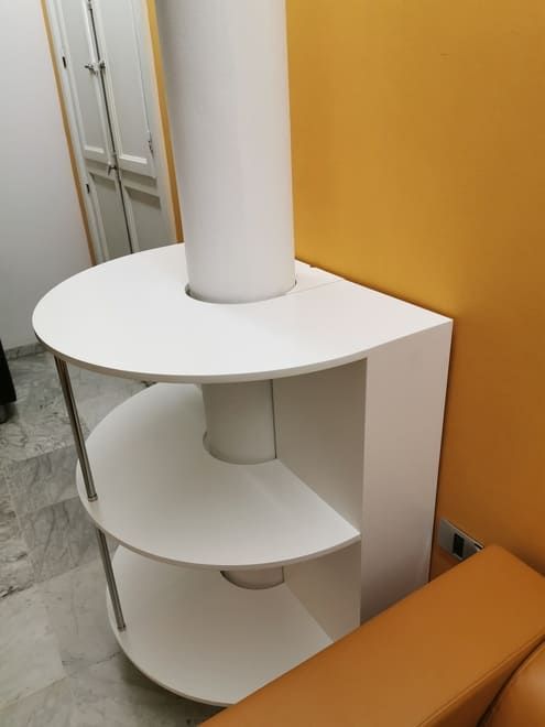 Estantería curva blanca alrededor de una columna junto a una pared naranja en una habitación interior.