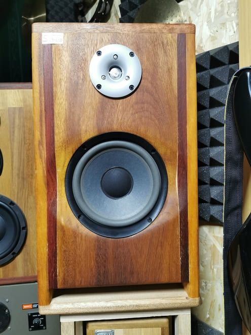 Altavoz de estantería de madera con woofer negro y tweeter plateado en un estudio de sonido.