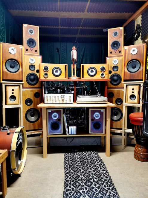 Habitación revestida de madera, repleta de altavoces apilados y equipos de audio en estantes y armarios.