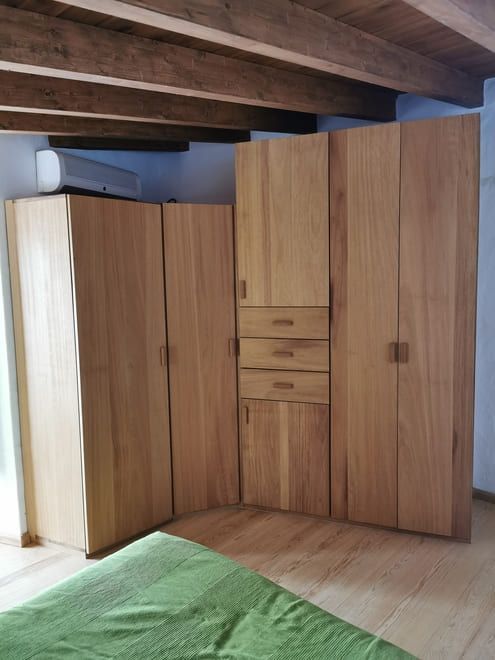 Armarios y gabinetes de madera en una pequeña habitación abuhardillada con vigas a la vista y una alfombra verde.