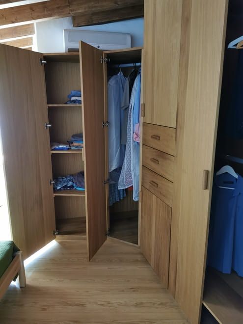 Armario abierto en un dormitorio, con ropa colgada, prendas dobladas y cajones bajo un techo inclinado.