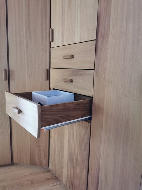 Armario de madera con un cajón abierto, que deja ver un cubo de basura azul en su interior.