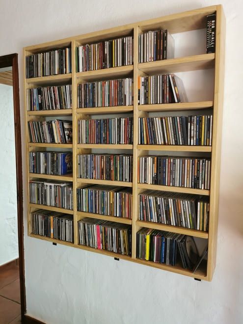 Estantería de madera con filas de CDs colocadas sobre una pared blanca.