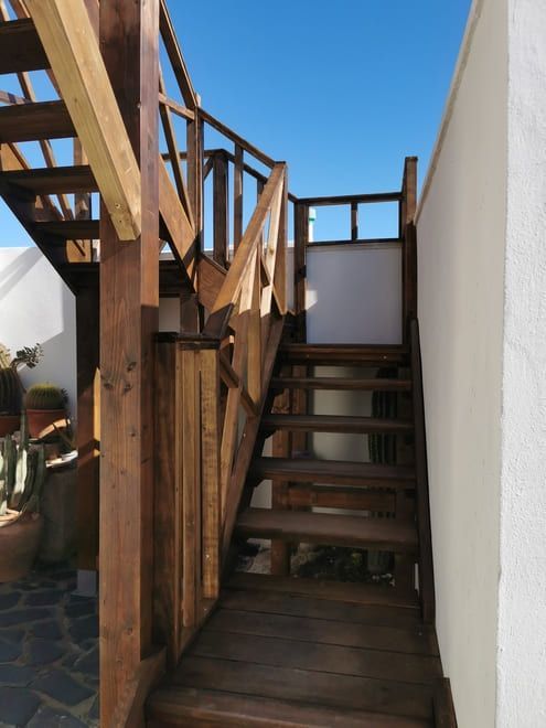 Una estrecha escalera de madera con barandillas entre paredes blancas bajo un cielo azul.