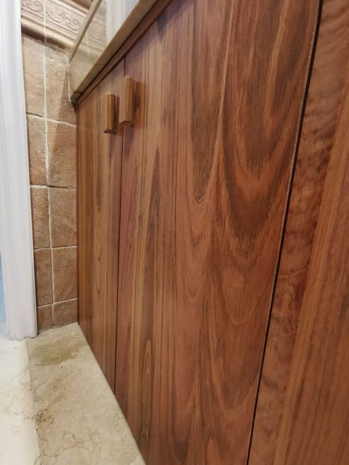 Mueble de baño con acabado de madera junto a una pared de ducha alicatada.