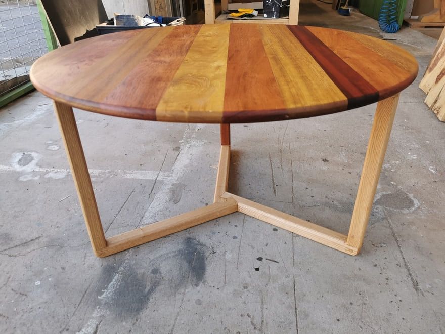 Mesa de centro redonda de madera con base de madera clara, ideal para un taller o garaje.