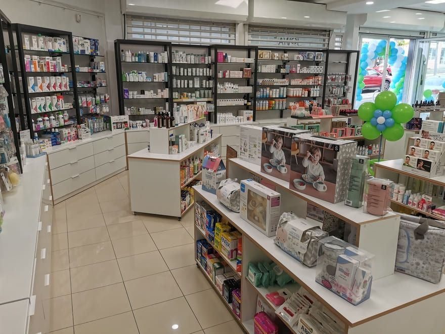 Interior luminoso de una farmacia o tienda de cosméticos con estantes blancos, expositores de productos y una decoración con globos de color verde azulado.