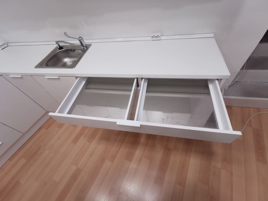 Cocina blanca con fregadero y armarios con cajones extraíbles abiertos debajo de la encimera.