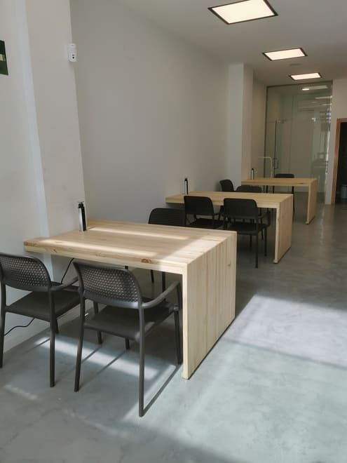 Pequeña oficina con escritorios y sillas negras en una habitación luminosa que parece un pasillo.
