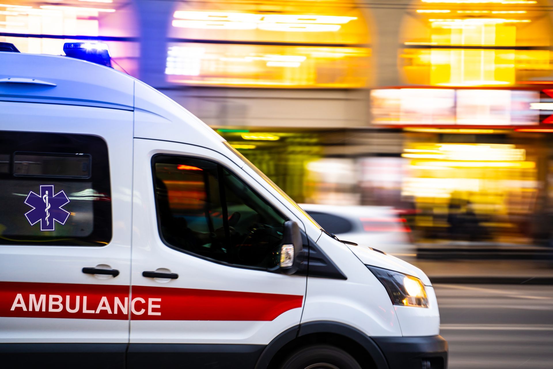 Ambulance avec gyrophares bleus allumés, roulant rapidement dans la rue.