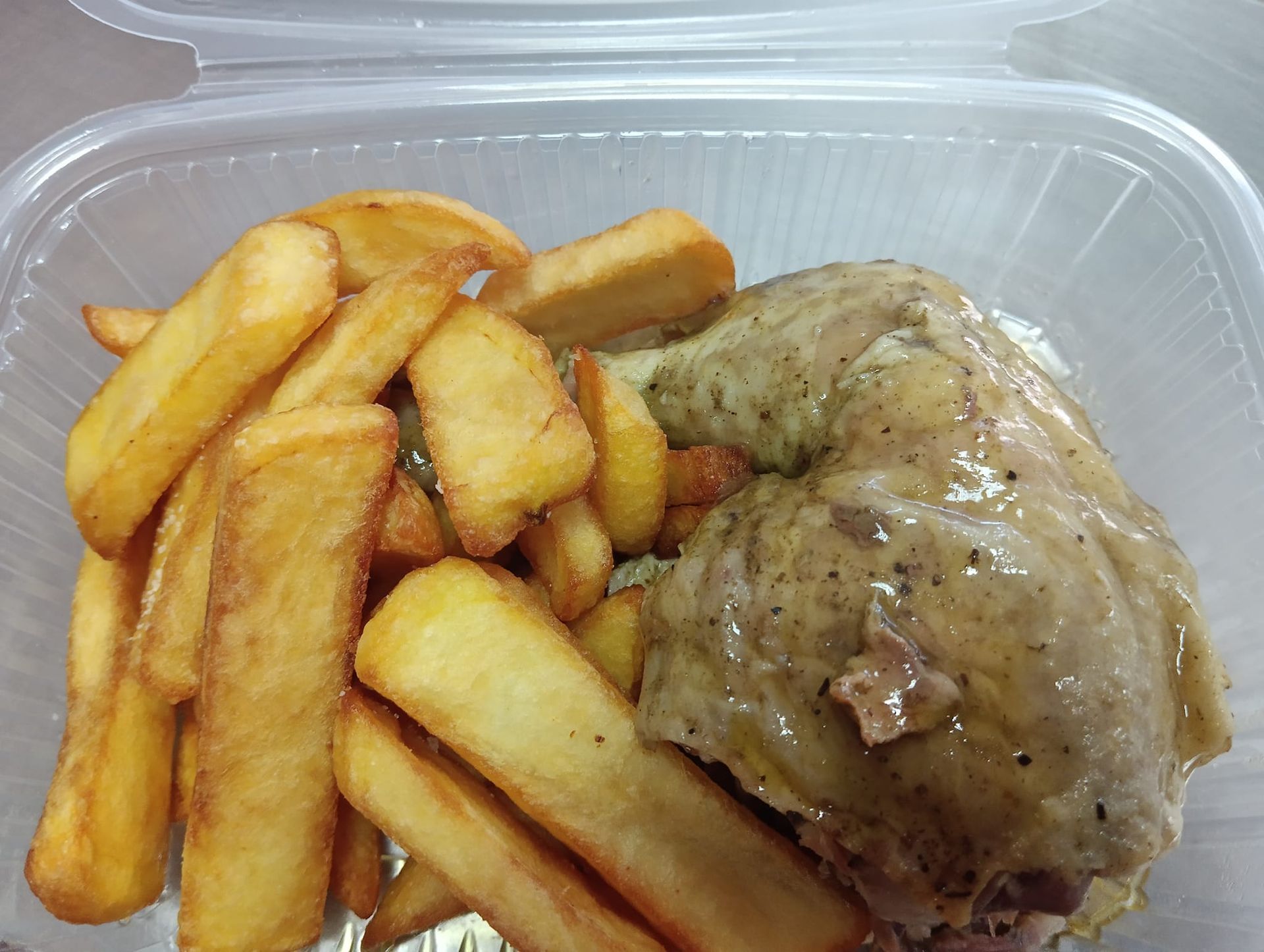Cuarto de pollo y papas fritas en un recipiente de plástico transparente para llevar.